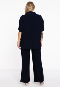 Navyblauwe twee-delige outfit met een losse top en brede broekspijpen. Zachte stof met een gladde textuur; het shirt heeft een kraag.