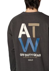 Szara bluza z dużą grafiką "ATW" w białym, beżowym i niebieskim kolorze, z napisem "OFF DUTY GEAR" poniżej w białym.