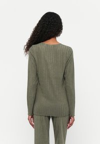 Olivegrünes, geripptes Langarmshirt mit Rundhalsausschnitt und strukturiertem Stoff. Es ist eng geschnitten und verfügt über Seitenschlitze für mehr Bewegungsfreiheit.