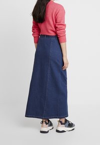 Mörkblå denim maxikjol med rak skärning, bakre sömsdetaljer och hög midja, kombinerad med en rosa tröja och sneakers.