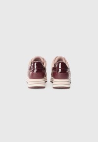Sneaker viola e beige con finitura lucida, forma arrotondata e suola a righe. Il tessuto testurizzato sul tallone aggiunge contrasto.