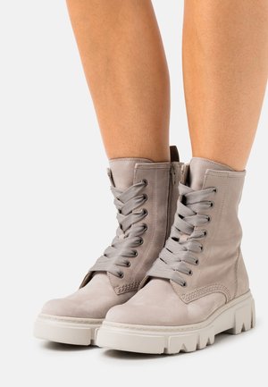 Bottines en suède gris à bout rond, avec un laçage à l'avant et une fermeture éclair. Caractéristiques d'une semelle en caoutchouc blanc épaisse et de coutures texturées.