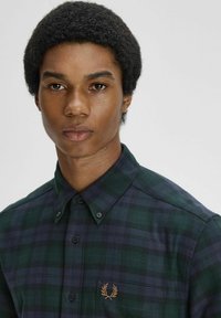 Camicia a quadri verde e blu navy con bottoni, realizzata in un tessuto dalla texture liscia. Presenta un piccolo logo ricamato sul petto.