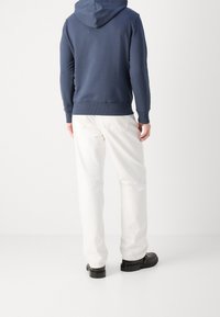 Felpa blu navy con cappuccio regolabile, polsini e orlo a costine, abbinata a pantaloni bianchi a gamba larga e calzature nere. Design semplice, vestibilità casual.