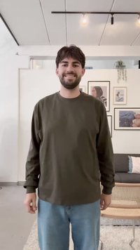 Tmavě zelená košile s dlouhým rukávem a kulatým výstřihem, kombinovaná se světle modrými džíny. Jednoduchý, ležérní design, látka vypadá měkká a pohodlná.