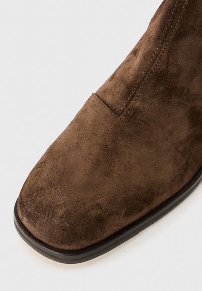 Brun mockaskinnsankleboots med en slät yta, fyrkantig tå och svart sula. Funkar utan extra mönster eller detaljer.