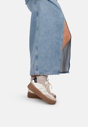 Person in a light blue denim skirt with a side slit wearing beige socks and white sneakers with brown soles and black heel accents.