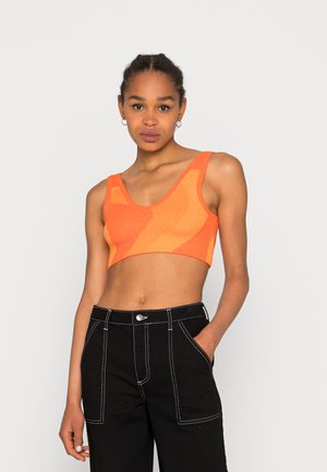 Top cropped de malha laranja com decote em V e alças largas, apresentando um padrão texturizado. Combinado com calças pretas de cintura alta com costura branca.