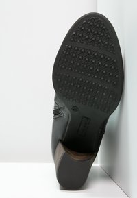Chaussure en cuir noir avec une semelle en caoutchouc texturé et un talon en bois. Détail élastique sur le côté pour un ajustement et un confort optimaux. Design à bout arrondi et plat.