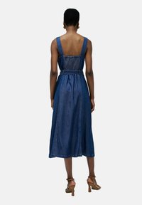 Vestido de mezclilla con un corsé ajustado y falda acampanada, con tirantes anchos, espalda fruncida y cintura ceñida con cinturón. Color azul oscuro, textura suave.