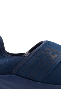 Scarpa sportiva navy con tomaia testurizzata, dettagli lisci, suola in gomma e un emblema logo. Le cuciture rinforzano la durata.
