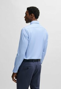 Camicia azzurro chiaro a maniche lunghe con una texture liscia e colletto a punta, abbinata a pantaloni blu scuro e una cintura nera.