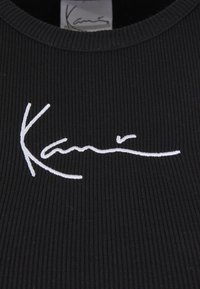 Fekete bordázott anyag fehér hímzett aláírás logóval. Kerek nyakkivágással és texturált felülettel rendelkezik.