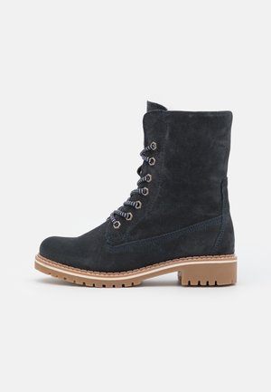 Bottine à lacets en daim noir avec semelle en caoutchouc marron clair et petit talon bloc, vue de profil sur fond uni.