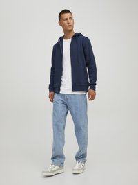 Sudadera con cremallera color navy de mezcla de algodón, con cordón y bolsillos frontales; llevada sobre una camiseta blanca, combinada con jeans de color azul claro y zapatillas blancas.