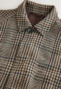 Kabát zo zmesi vlny s kockovaným vzorom v hnedých, krémových a multicolor akcentoch. Obsahuje špicatý golier a jedno čierne zapínanie na gombík.
