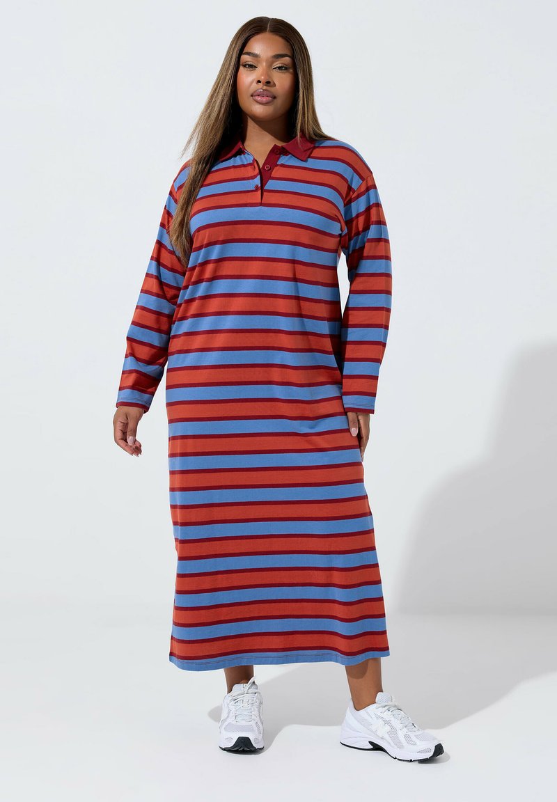 Czerwona i niebieska w paski długa sukienka z kołnierzykiem i długimi rękawami, w połączeniu z białymi butami sportowymi. Teksturowana tkanina.