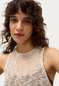 Top senza maniche lavorato a maglia beige con un design a trama aperta texturizzata, scollatura rotonda e tessuto liscio sotto in un colore scuro a contrasto.
