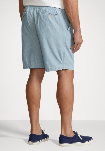 Lyseblå chambray-shorts med elastisk talje, sidelommer og en baglomme med knap. Bæres med navy canvas-sko.