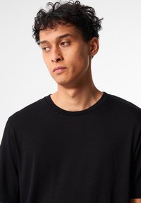 Schwarzes T-Shirt mit kurzen Ärmeln und rundem Halsausschnitt, mit lockerem Schnitt, gefertigt aus einem glatten, leichten Stoff mit minimaler Textur.