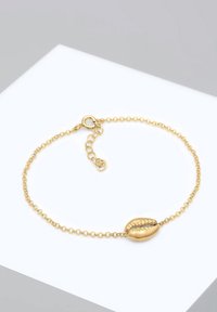 Guld kedjebraccialett med en cowrie snäcka charm, slät yta och justerbar längd med spänne.