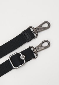 Sort nylonrem med metalhardware, der har to clips og en cirkulær detalje prægede med "Kipling." Tekstureret overflade med solidt design.