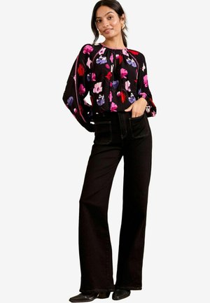 Blusa nera a fiori con fiori multicolori, scollatura arricciata e maniche morbide. Abbinata a jeans neri a vita alta a zampa e calzature nere.