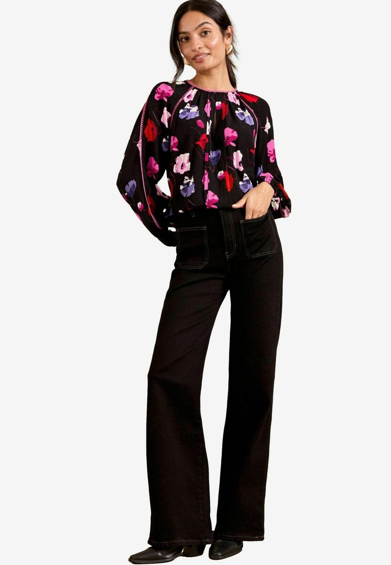 Blusa nera a fiori con fiori multicolori, scollatura arricciata e maniche morbide. Abbinata a jeans neri a vita alta a zampa e calzature nere.