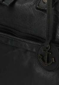 Bolso de cuero negro con cierre de cremallera, que presenta un emblema de ancla redondo y una superficie texturizada. El diseño incluye un asa superior y detalles de costura.