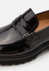 Mocassins en cuir verni noir avec un upper texturé, featuring deux bandes décoratives et une semelle en caoutchouc striée. Doublure intérieure lisse.