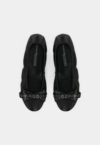 Chaussures plates noires avec une finition satinée, bout arrondi et détail en nœud noir avec œillets en métal argenté. Tissu doux et doublure intérieure lisse.