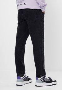 Vaqueros de mezclilla negros con un corte slim, que presentan un diseño clásico de bolsillos. Combinados con zapatillas negras y blancas con detalles en púrpura.