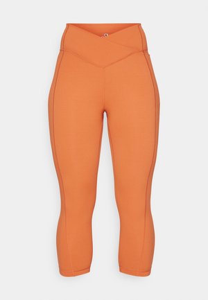 Oransje capri leggings laget av elastisk stoff. Har et høyt, crossover liv og kontrastsømmer langs sidene.
