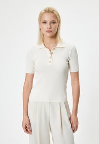 Geribbelde witte polo met korte mouwen, uitgerust met een kraag en drie gouden knopen aan de voorkant. Gladde stof, getailleerd ontwerp.