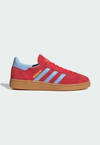 Červené tenisky Adidas Spezial s svetlomodrými pruhmi, gumenou podrážkou a žltým brandingom na boku, zobrazené z profilu na bielom pozadí.