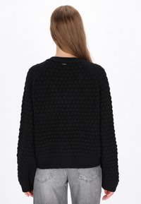 Czarny sweter z dzianiny z teksturowanym wzorem w bobble, szerokimi rękawami i ściągaczem u dołu. Luźny krój z prostym okrągłym dekoltem.