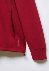 Manche longue rouge de sweat-shirt avec poche sur le côté et cordon de serrage ajustable à l'ourlet, étiqueté "MNS Performance."