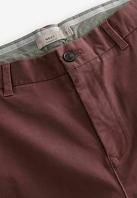 Pantalon droit bordeaux avec une texture lisse, présentant un bouton de fermeture et une ceinture intérieure à motifs. Étiquette visible à l'intérieur.