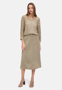 Pull en tricot beige avec un col en V et une coupe ample, associé à une jupe khaki uni arrivant au genou, avec des poches frontales et une silhouette épurée.