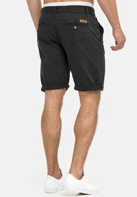 Shorts noirs en coton avec ourlets retroussés, dotés de poches latérales et arrière, d'un écusson en cuir avec logo, assortis à des baskets blanches.