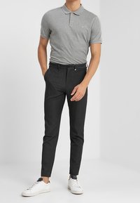 Polo gris à manches courtes, pantalon noir ajusté et baskets blanches. La tenue comporte un logo de marque discret sur le polo.