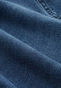 Tejido de mezclilla azul oscuro con una textura suave, que presenta un ligero desgastado y un patrón de tejido diagonal, doblado en múltiples capas.