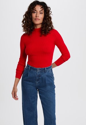 Maglia a maniche lunghe rossa a coste abbinata a jeans blu in denim a vita alta. La maglia presenta un design aderente e un collo alla coreana.