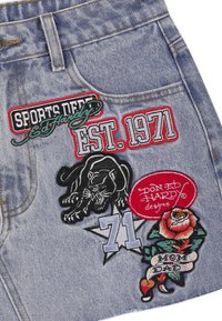 Tessuto di denim con toppe ricamate tra cui una pantera nera, una rosa con striscione "Mom Dad", la scritta "EST. 1971" e il testo "Don Ed Hardy designs".