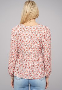 Blusa floreale con maniche lunghe a sbuffo, caratterizzata da una vita arricciata. Il motivo presenta piccoli fiori rossi e rosa su uno sfondo chiaro.