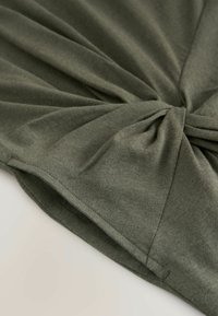 Olivgrünes Baumwolloberteil mit einer verdrehten Vorderseite, glatter Textur und drapiertem Stoff mit weichen Nähten.