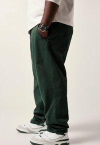 Groene katoenen broek met zijzakken, relaxed fit, gecombineerd met witte en groene sportschoenen. Beschikt over een casual ontwerp en een gladde textuur.