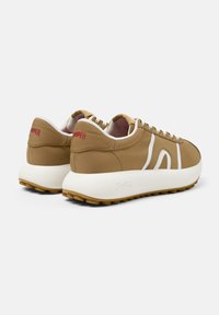 Sneaker marrone con accenti bianchi e suola in gomma. Presenta un collare imbottito, lacci a contrasto e il logo "Camper" sul tallone.