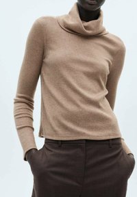 Pull beige à côtes avec un col cheminée, des manches longues et un ourlet légèrement court, associé à un pantalon marron plissé. Texture lisse et douce.