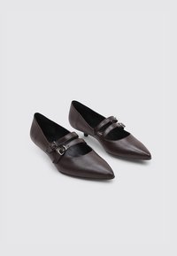 Mocasines de cuero marrón de punta afilada con dos correas ajustables con hebillas a través del empeine y un tacón bajo, que presentan una textura suave.